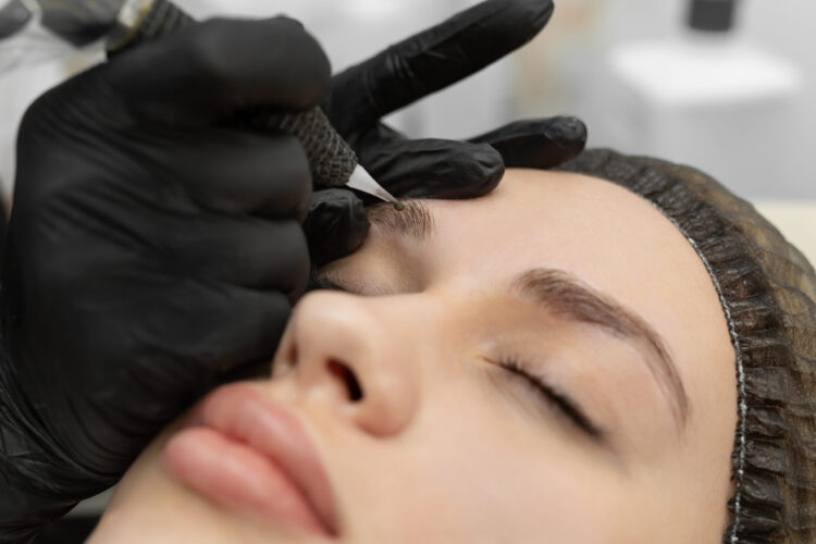 Concept of microblading eyebrows. The cosmetologist performs the procedure of permanent makeup of the eyebrows in close-up.